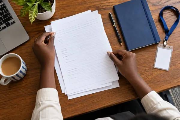 Hands holding employment papers beside a cup of tea and an ID badge