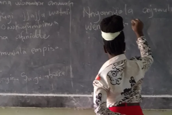 A teacher writing a lesson in Luganda on a classroom blackboard