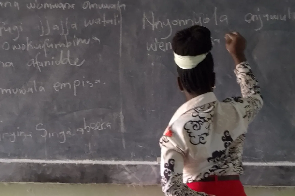 A teacher writing a lesson in Luganda on a classroom blackboard