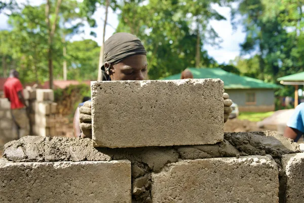 A builder placing a concrete block on a wall at an outdoor construction site in Mukono